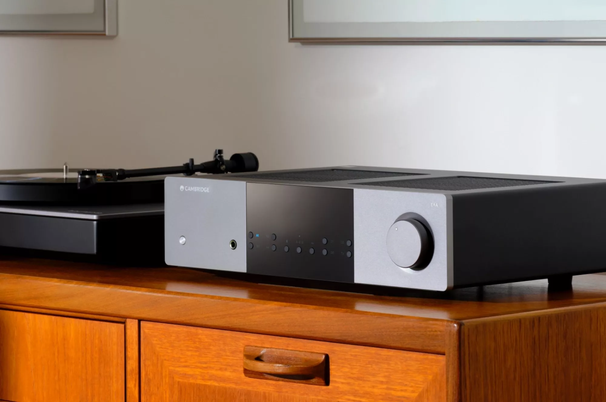 Cambridge Audio EXA100 vedle gramofonu na teakové komodě, frézovaný hliníkový panel a velký kruhový knoflík hlasitosti