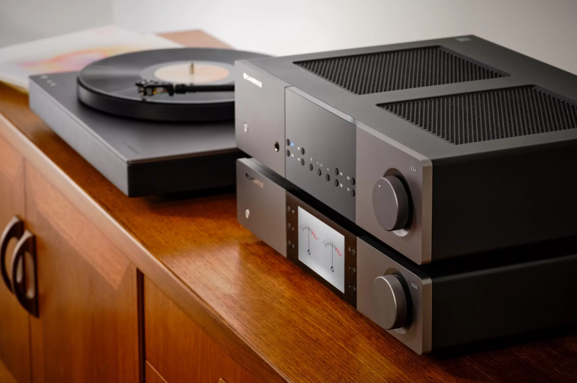 Cambridge Audio EXN100 a zesilovač EXA100 naskládané na sobě na dřevěné komodě vedle gramofonu s deskou