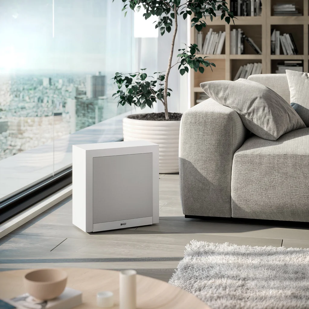 KEF T2 v bílém provedení postavený na podlaze vedle světlé pohovky v obýváku s výhledem do města