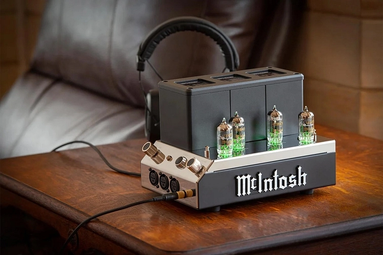 McIntosh MHA200 se zeleně podsvícenými elektronkami na dřevěném stolku vedle kožené sedačky a sluchátek