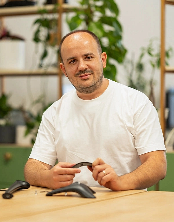 Produktový designér Meze Audio Szabolcs Ferenczi u pracovního stolu s dílem stojanu Manta v ruce