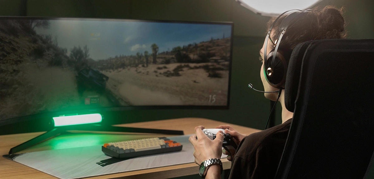 Hráč se sluchátky Meze Audio a nasazeným mikrofonem Boom Mic u zakřiveného herního monitoru