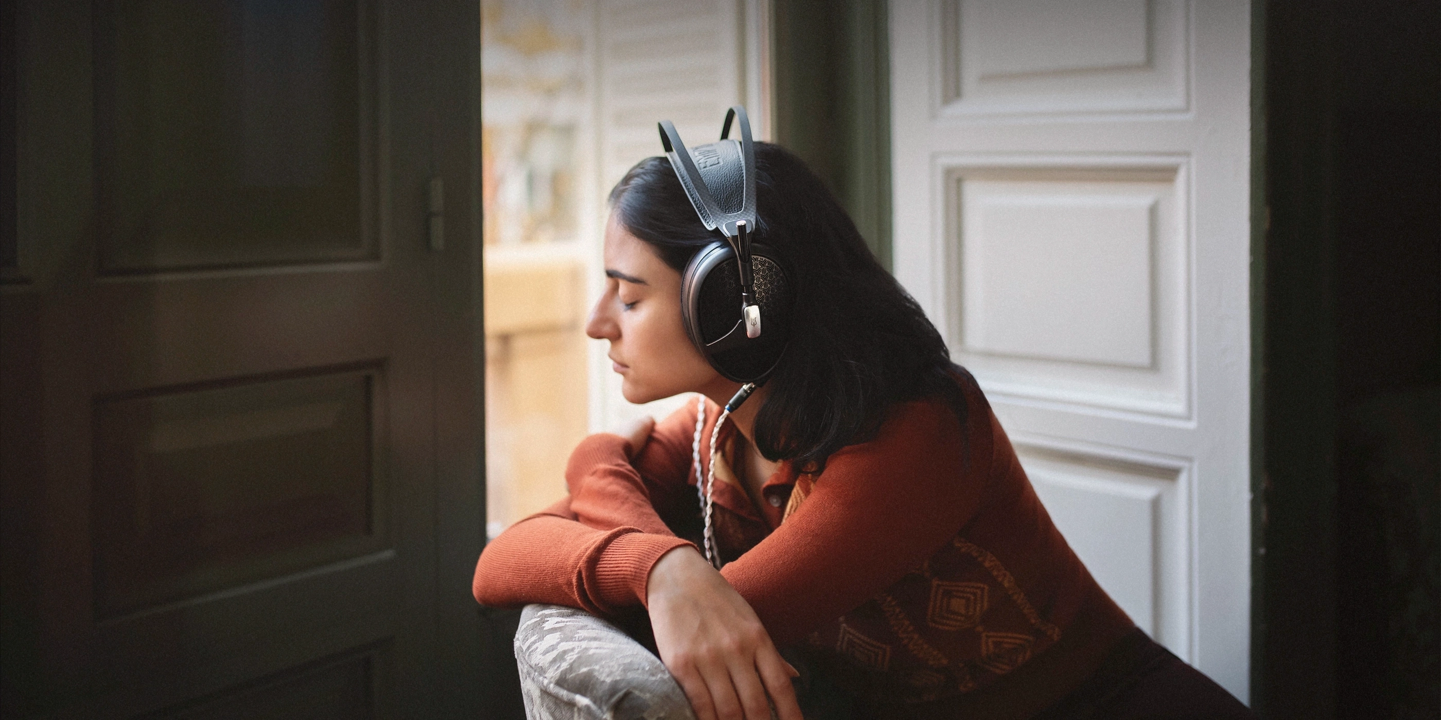 Žena s nasazenými otevřenými sluchátky Meze Audio Empyrean II v tlumeném interiéru