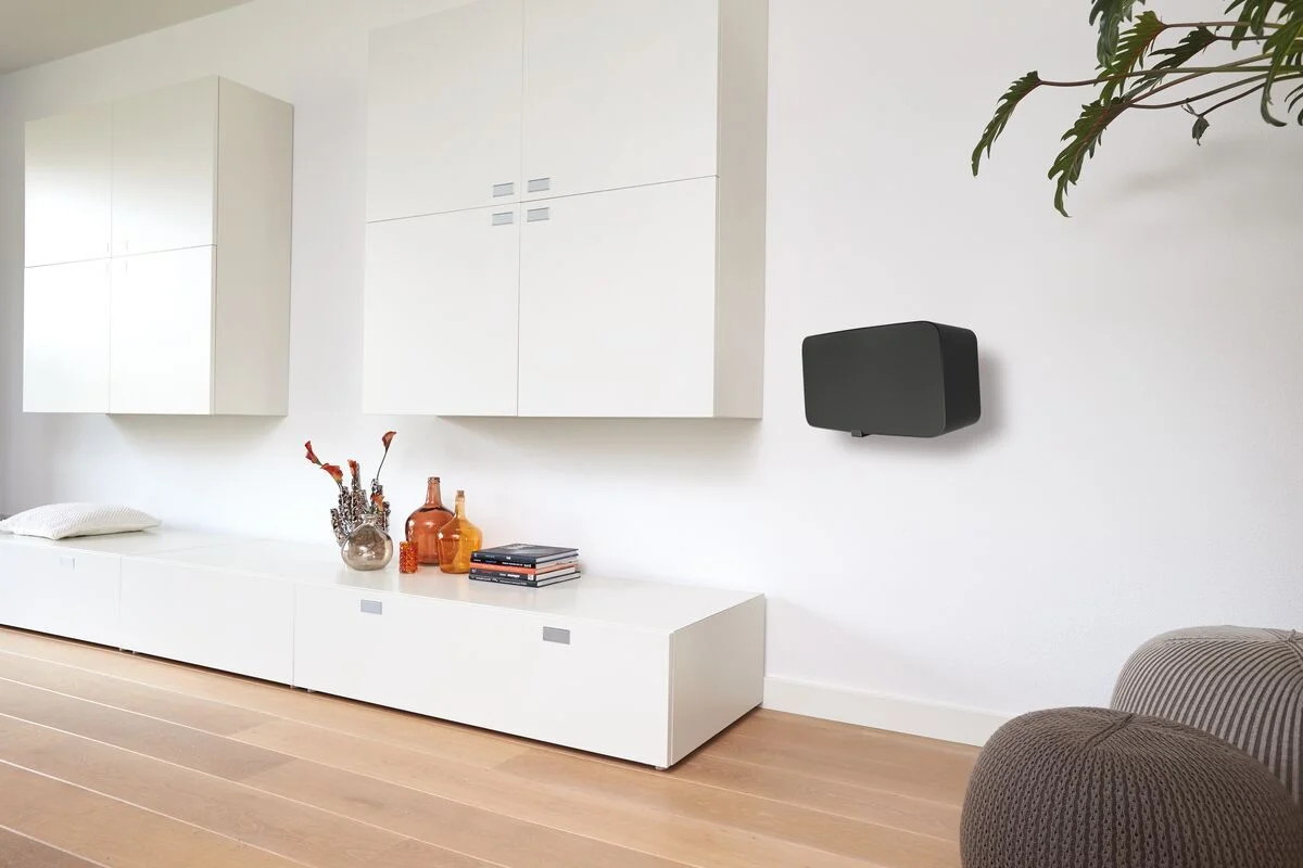 Černý reproduktor Sonos na nástěnném držáku Vogel's SOUND 3205 ve světlém obývacím pokoji s bílým nábytkem a dřevěnou podlahou