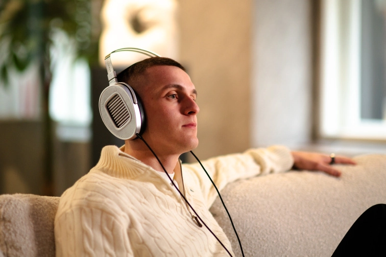 Posluchač z profilu na pohovce se sluchátky HIFIMAN HE1000 Unveiled, otevřené mušle s viditelnou planárně-magnetickou membránou