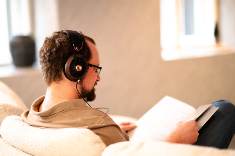 Posluchač v křesle se sluchátky Meze Audio 109 Pro při čteni knihy v tlumeném světle