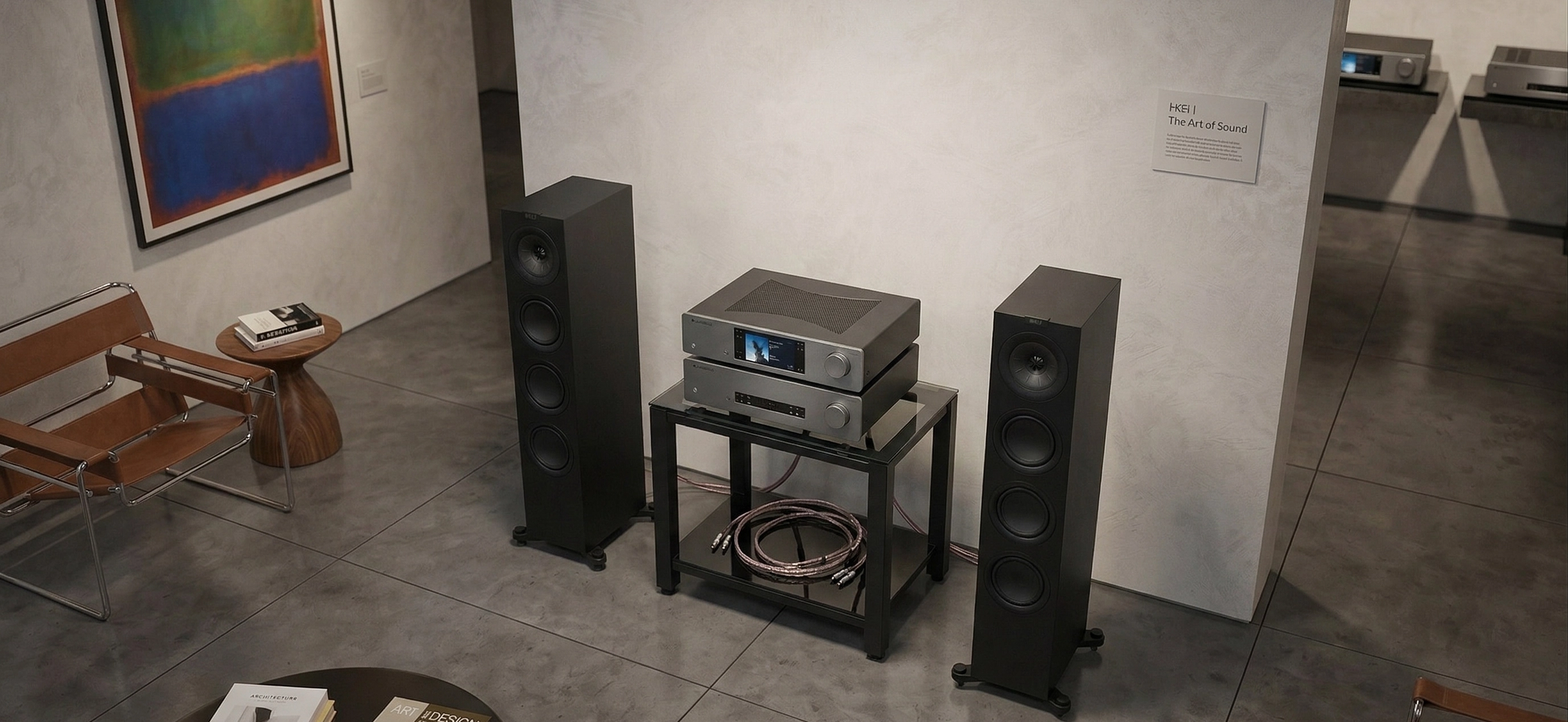 Širší pohled na obývací pokoj se sestavou VOIX Signature INTENSITY — černé podlahovky KEF, elektronika Cambridge Audio na skleněném stolku a smyčka kabeláže Nordost Red Dawn 3