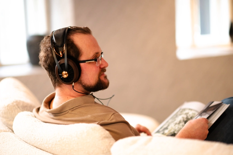 Posluchač z profilu se sluchátky Meze Audio 109 Pro, soustředěný poslech vsedě s časopisem