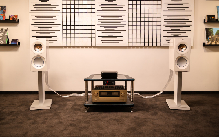 VOIX Reference PRIME v showroomu — pár bílých regálovek KEF Reference 1 Meta na stojanech, mezi nimi nízký stolek se zlatým zesilovačem Accuphase E-4000 a streamerem, akustické difuzory na stěně