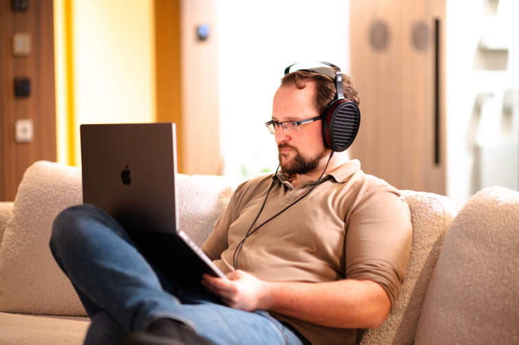 Muž poslouchá hudbu se sluchátky HIFIMAN na pohovce, na klíně notebook
