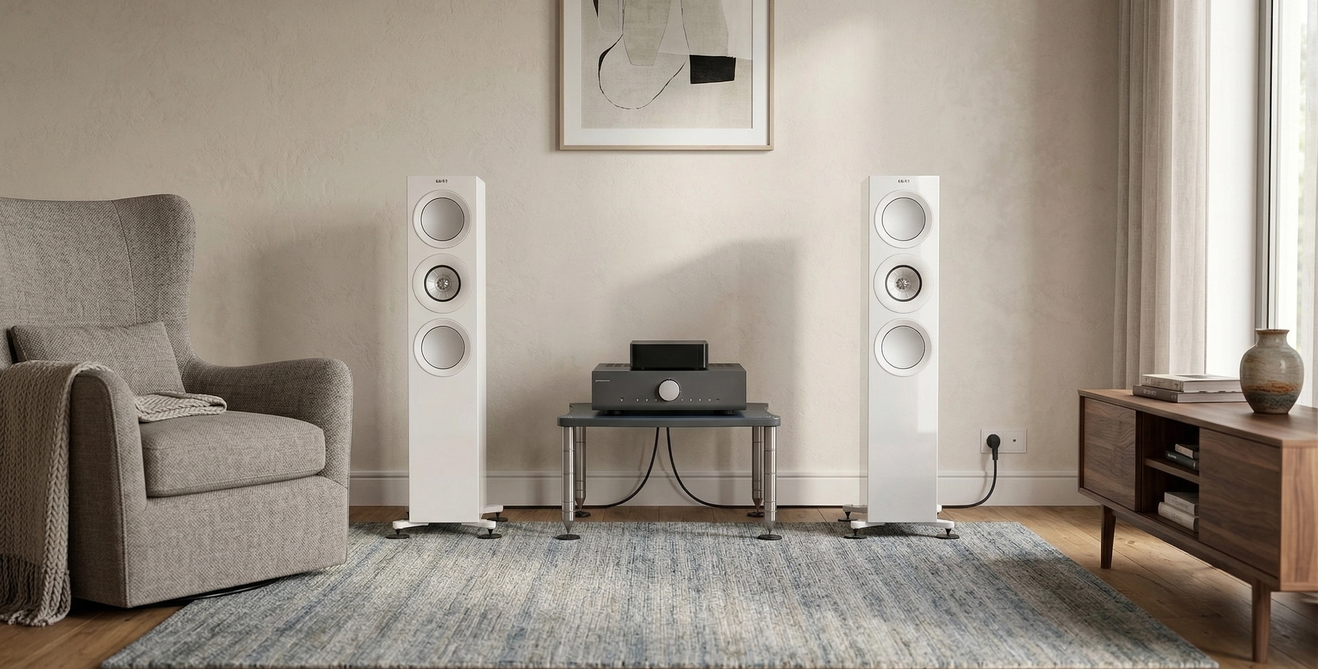 Bílé podlahovky KEF R7 Meta v útulném obývacím pokoji se šedým křeslem a elektronikou sestavy na nízkém stolku