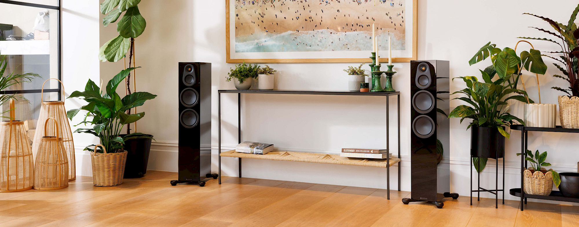 Pár sloupových reprosoustav Monitor Audio Silver 300 8G v provedení High Gloss Black po stranách konzolového stolku v prosvětleném obývacím pokoji s pokojovými rostlinami