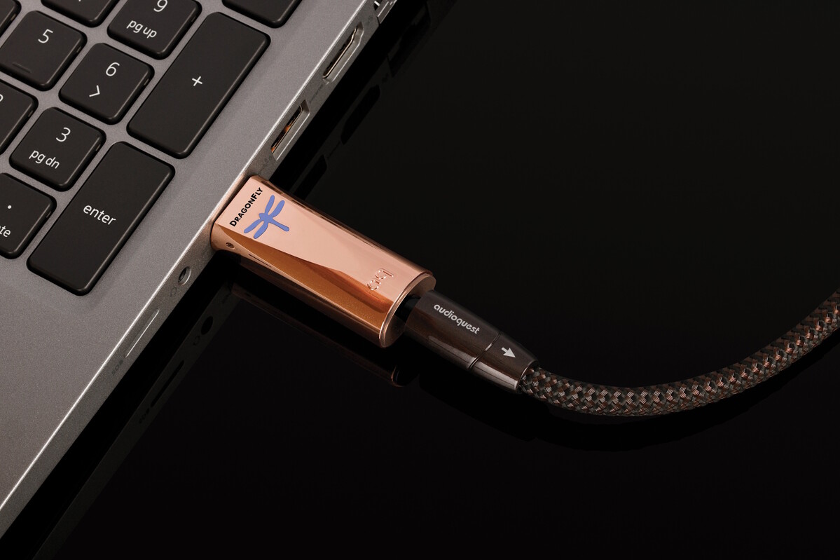 DragonFly Copper zasunutý přímo do USB-A portu notebooku, s modře svítící vážkou a opleteným kabelem sluchátek