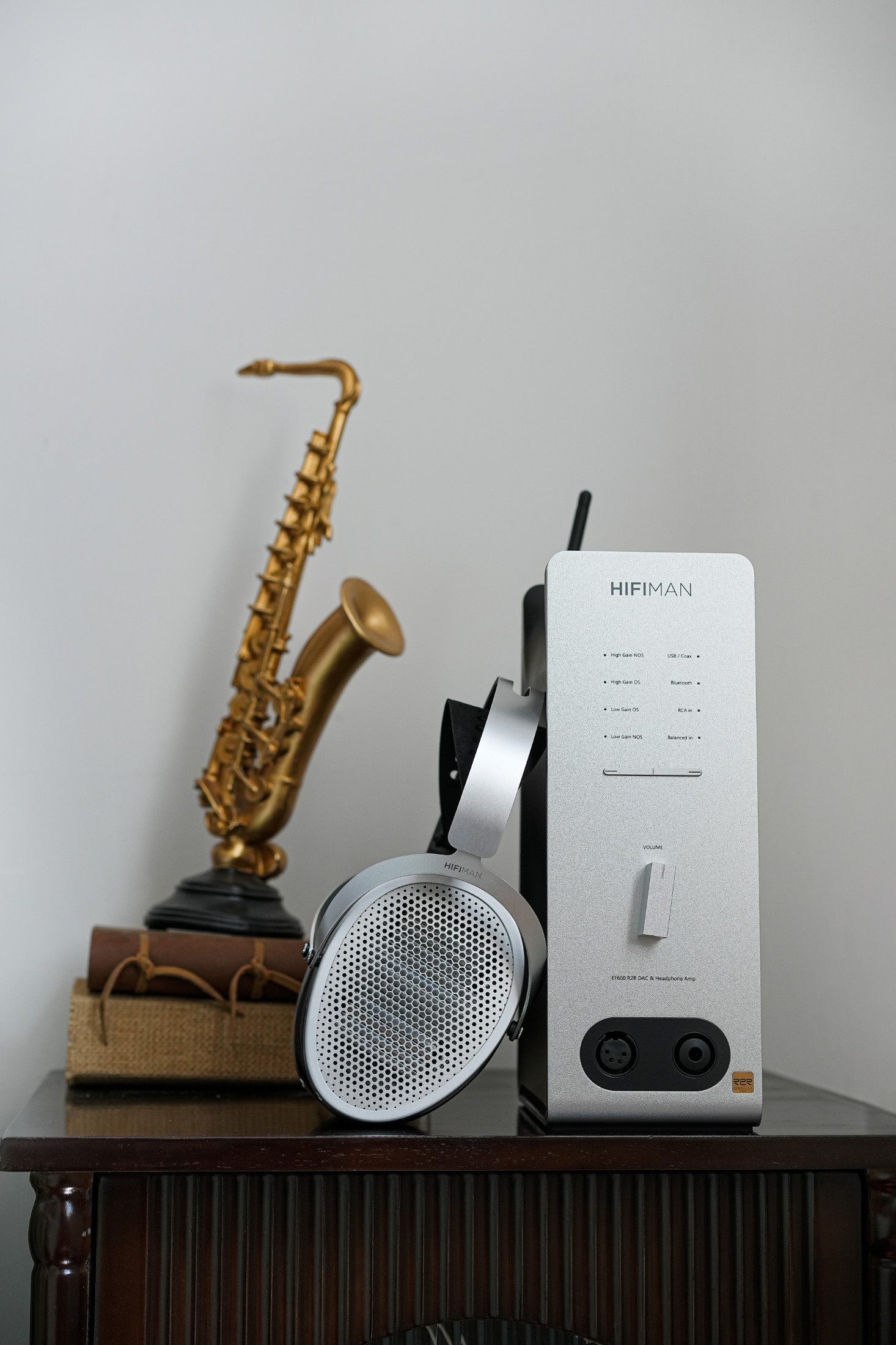 Sluchátka HIFIMAN Edition XV opřená o zesilovač HIFIMAN EF600 vedle zlaté sošky saxofonu a svázaných knih