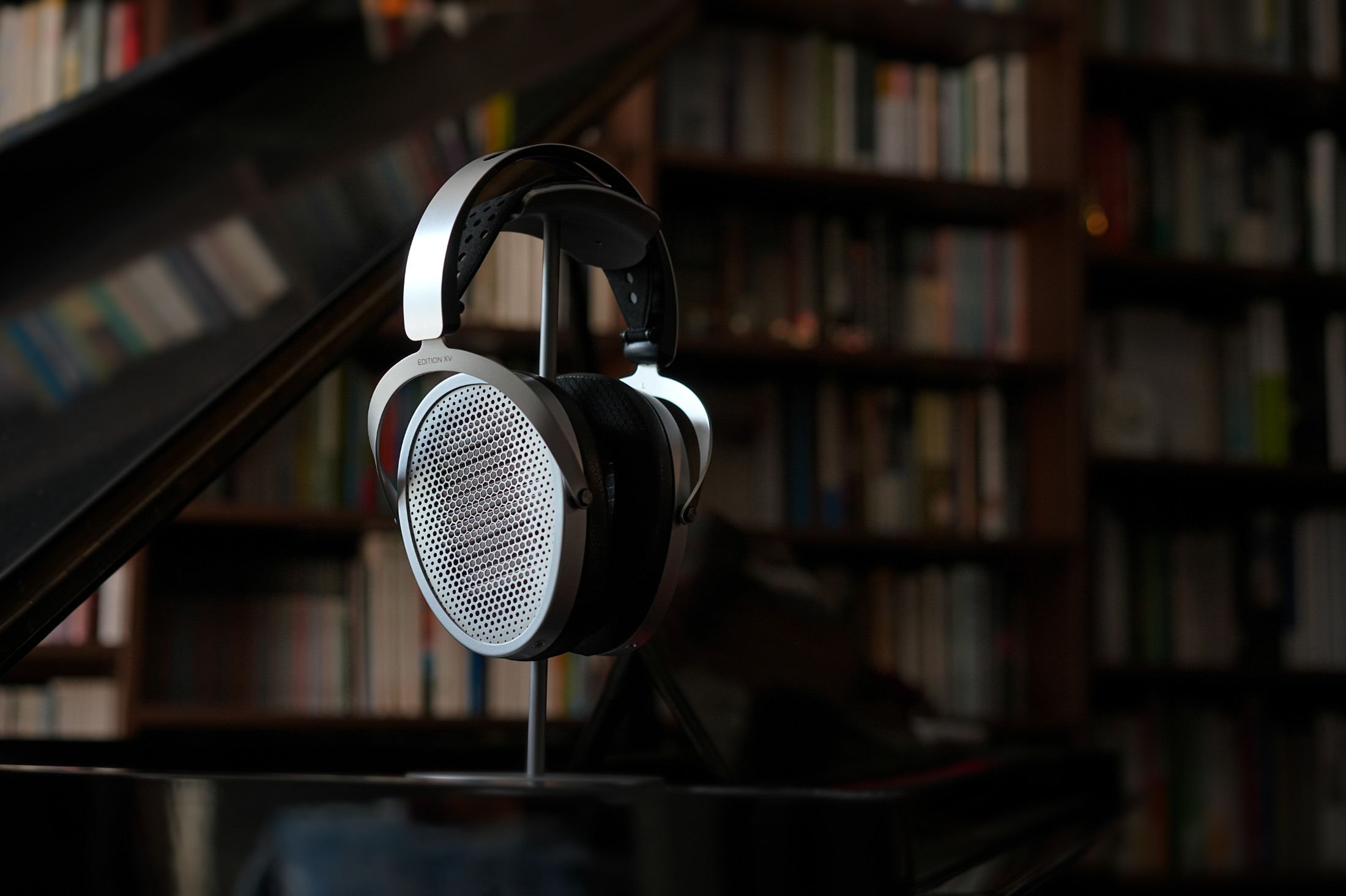 Sluchátka HIFIMAN Edition XV na kovovém stojanu na křídle, v pozadí stěna plná knih