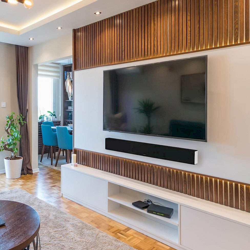 Černý soundbar Monitor Audio pod televizorem na stěně s dřevěným lamelovým obkladem
