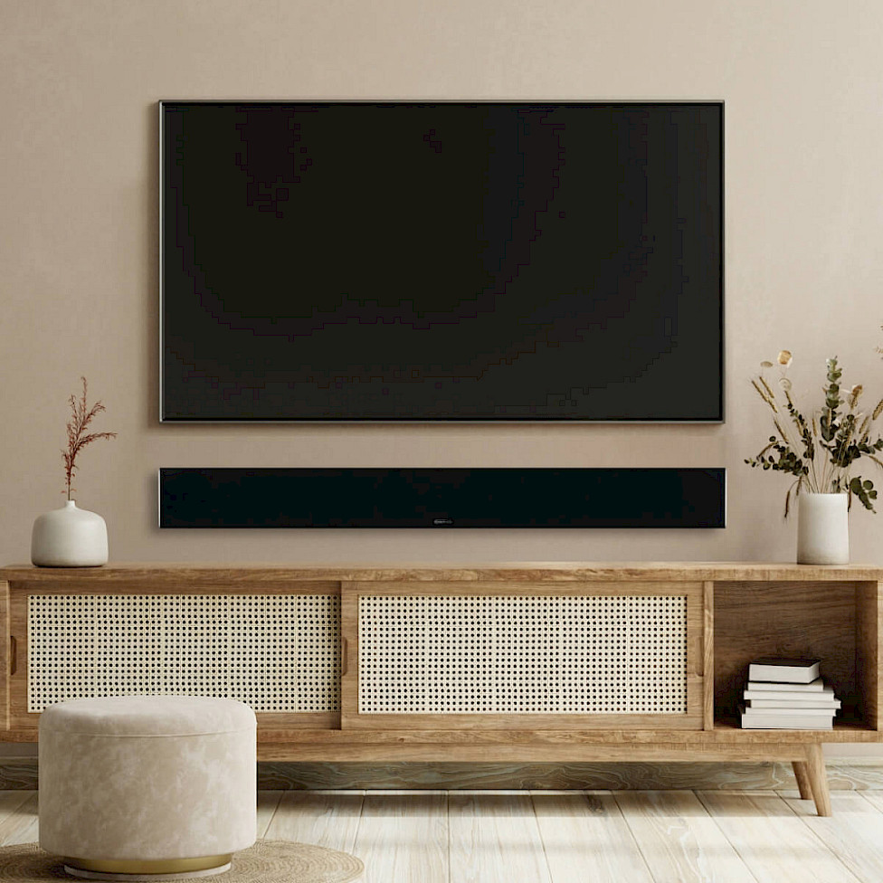Soundbar Monitor Audio pod televizorem na béžové stěně nad ratanovou komodou