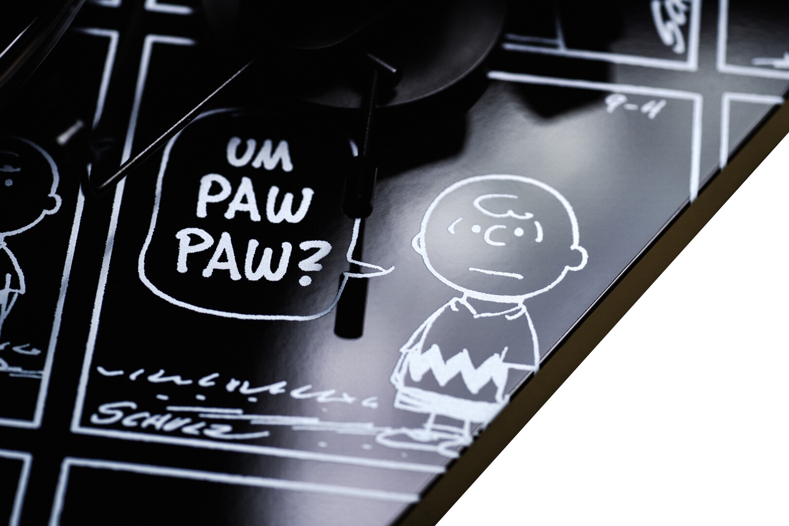 Detail komiksového potisku horní desky s bublinou UM PAW PAW? a kresbou Charlieho Browna