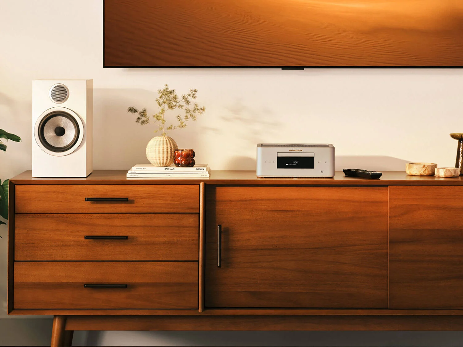 Marantz MCR 60n DAB v provedení Champagne Gold na dřevěné komodě pod televizí vedle regálového reproduktoru a dálkového ovladače