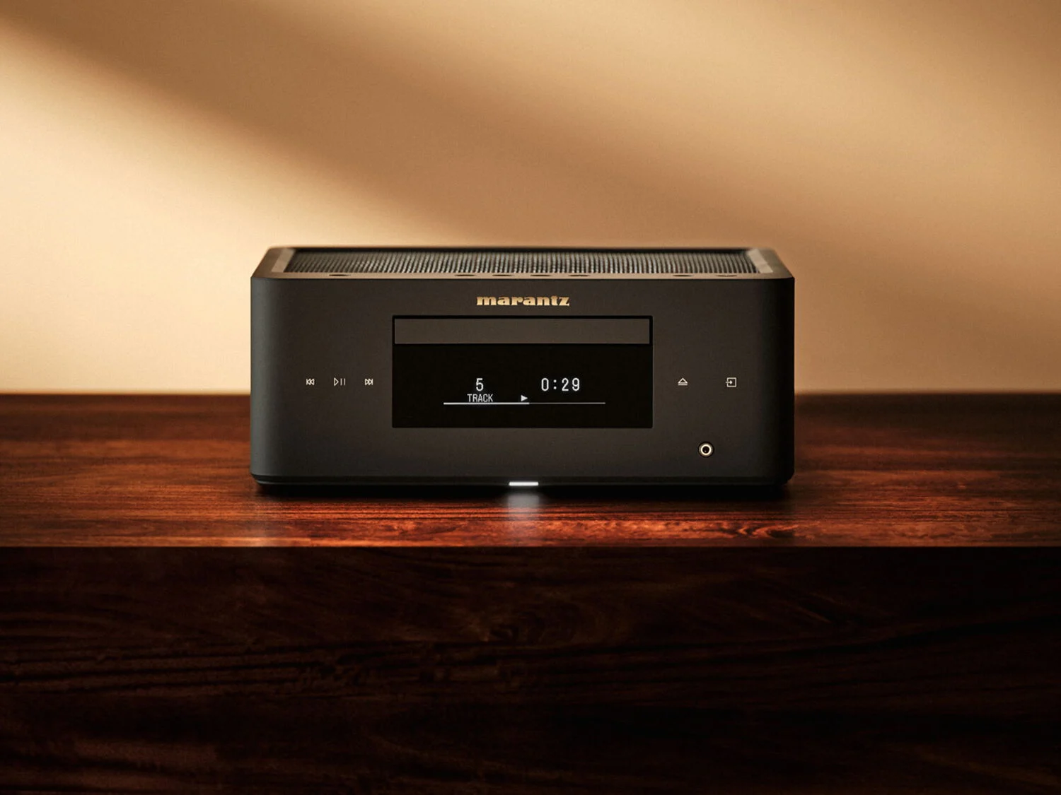 Marantz MCR 60n DAB v černém provedení na dřevěné komodě před teple nasvícenou stěnou, na displeji běží pátá stopa CD