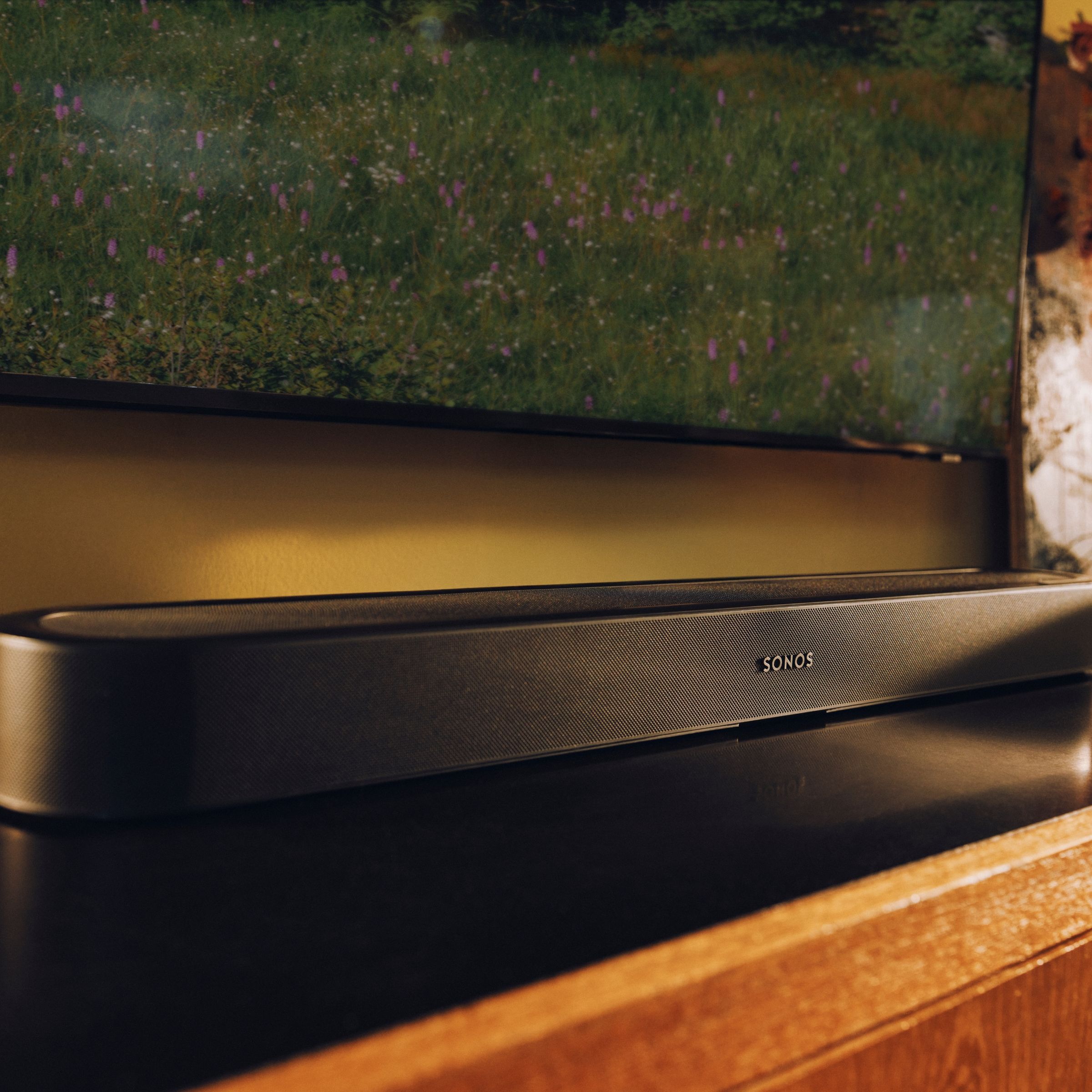 Hero foto 16:9: Sonos Beam Ultra pod plochou televizí v obývacím pokoji, večerní scéna s puštěným filmem