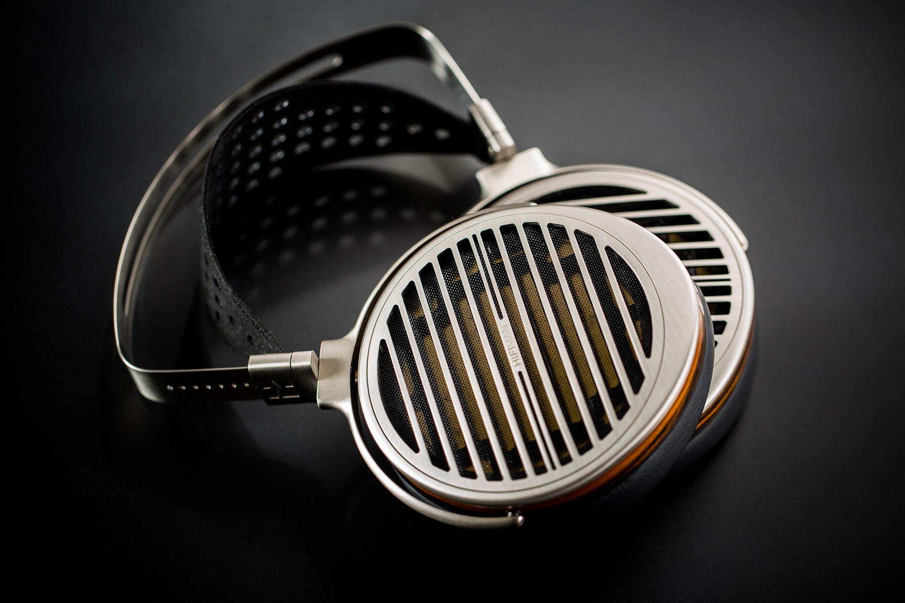 HIFIMAN Susvara na tmavém pozadí — celkový pohled na otevřenou konstrukci s kovovou mřížkou a děrovaným koženým páskem