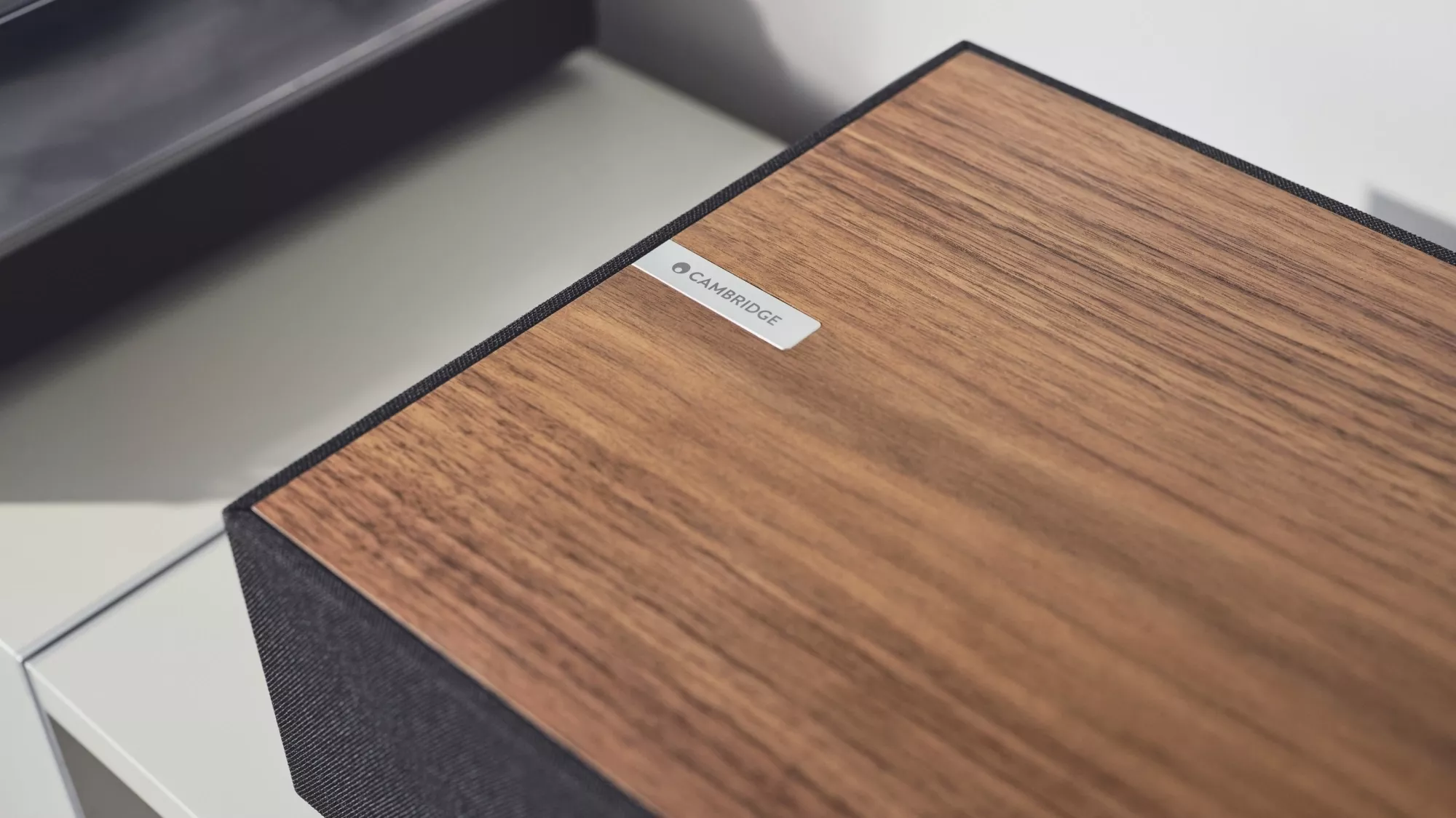 Detail ořechového dřevěného vrchu Cambridge Audio Evo One s kovovým štítkem Cambridge a tmavou látkovou maskou