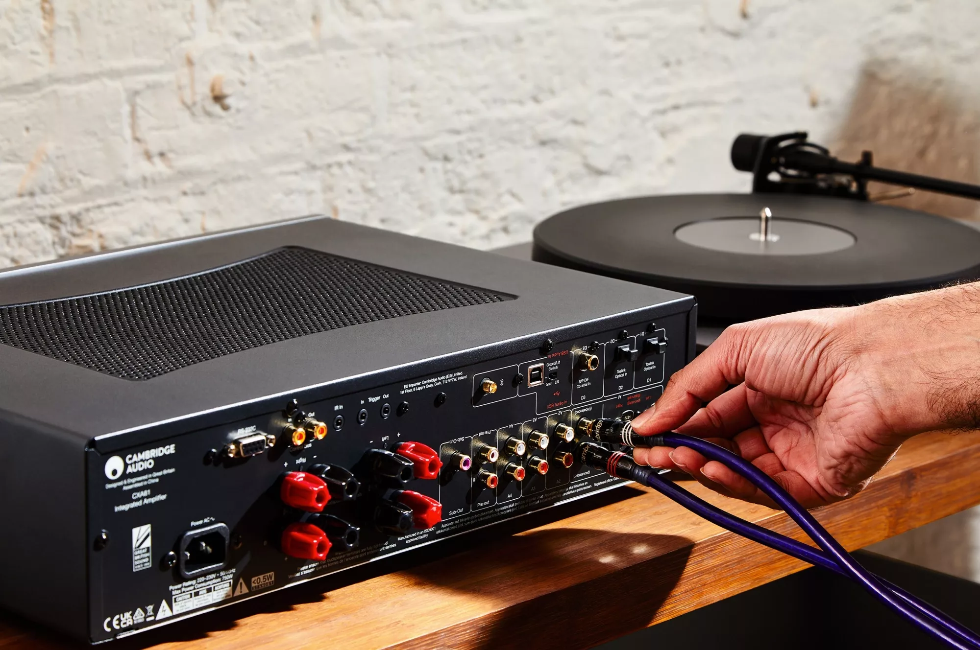 Zadní panel Cambridge Audio CXA81 Mk II s reproduktorovými terminály a digitálními vstupy, ruka zapojuje kabely