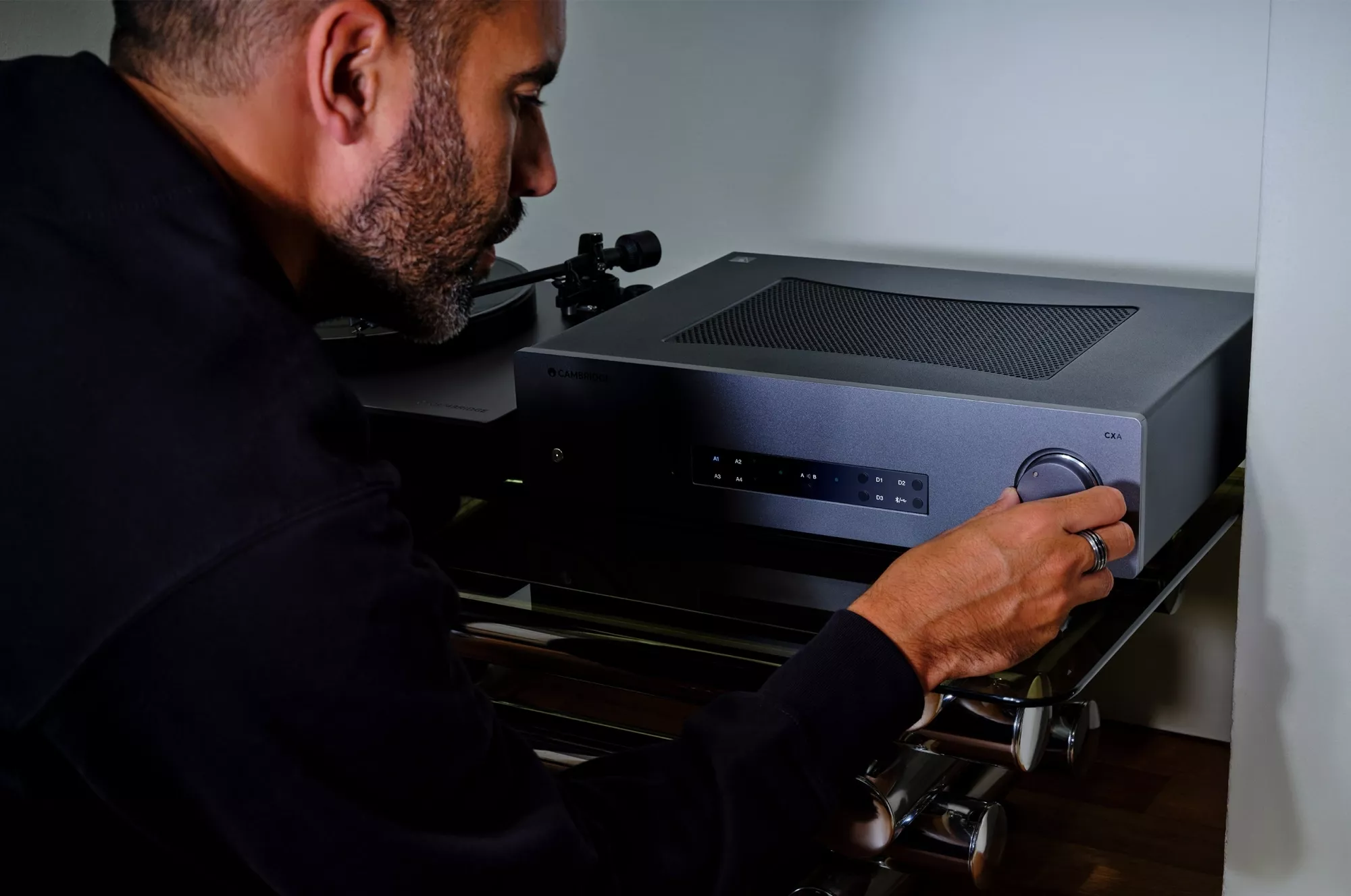 Muž ladí hlasitost na čelním knoflíku Cambridge Audio CXA81 Mk II při poslechu gramofonu
