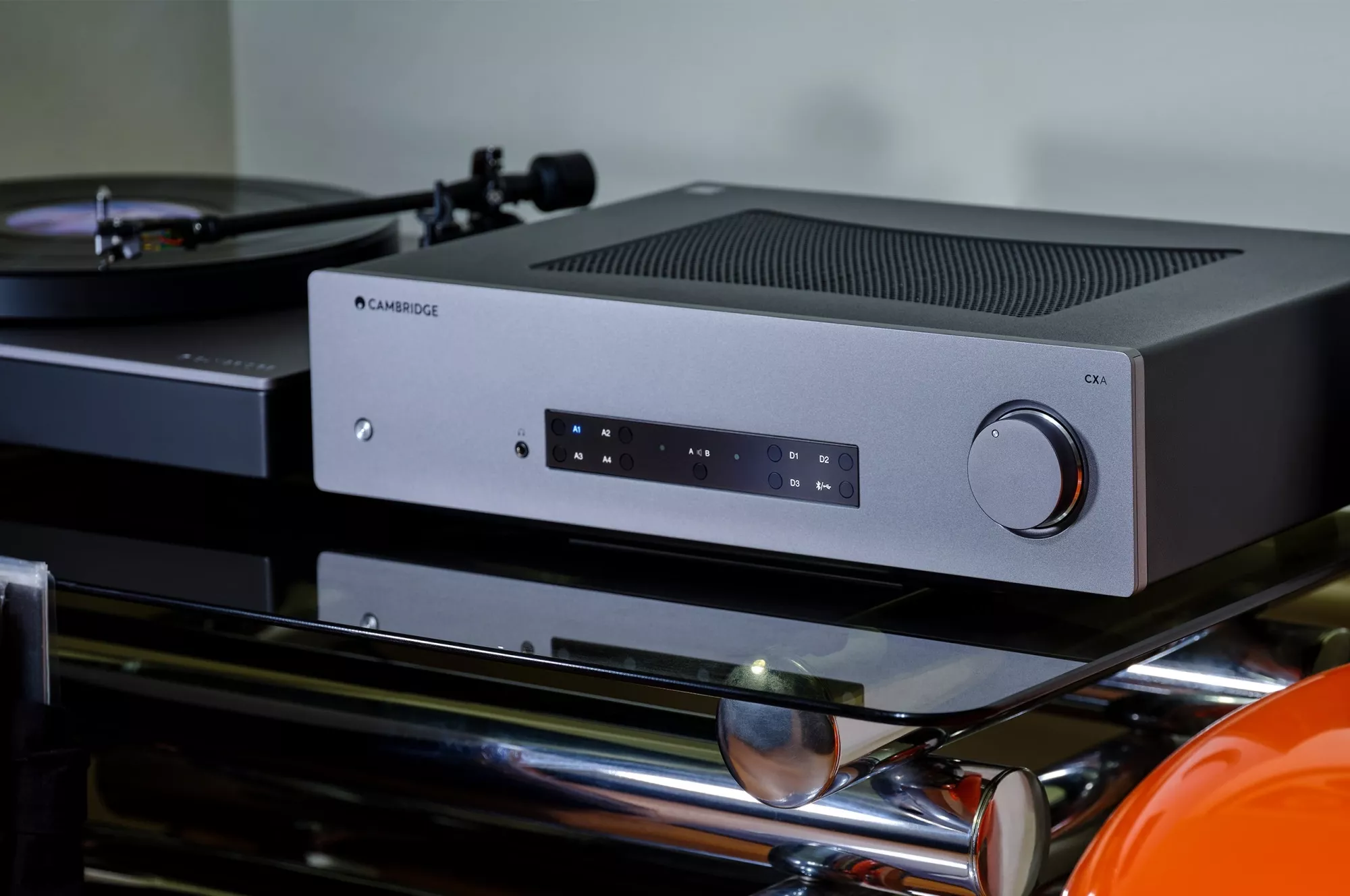 Stříbrný Cambridge Audio CXA81 Mk II na skleněném stojanu vedle gramofonu