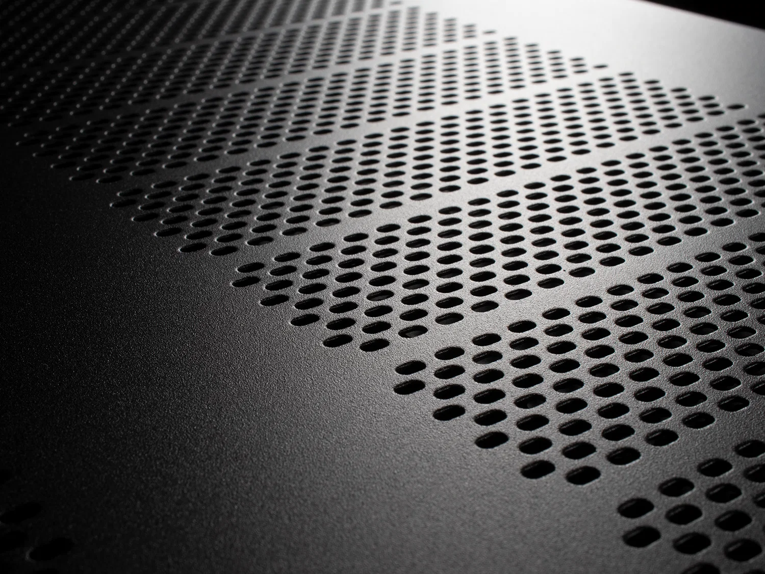 Detail perforovaného horního krytu zesilovače Emotiva BasX v šikmém světle