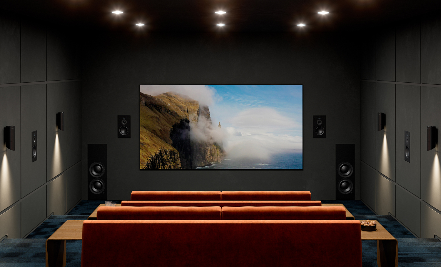 Domácí kino s vestavnými reproduktory Lyngdorf po stranách velké obrazovky i na bočních stěnách, tři řady rezavě oranžových sedaček