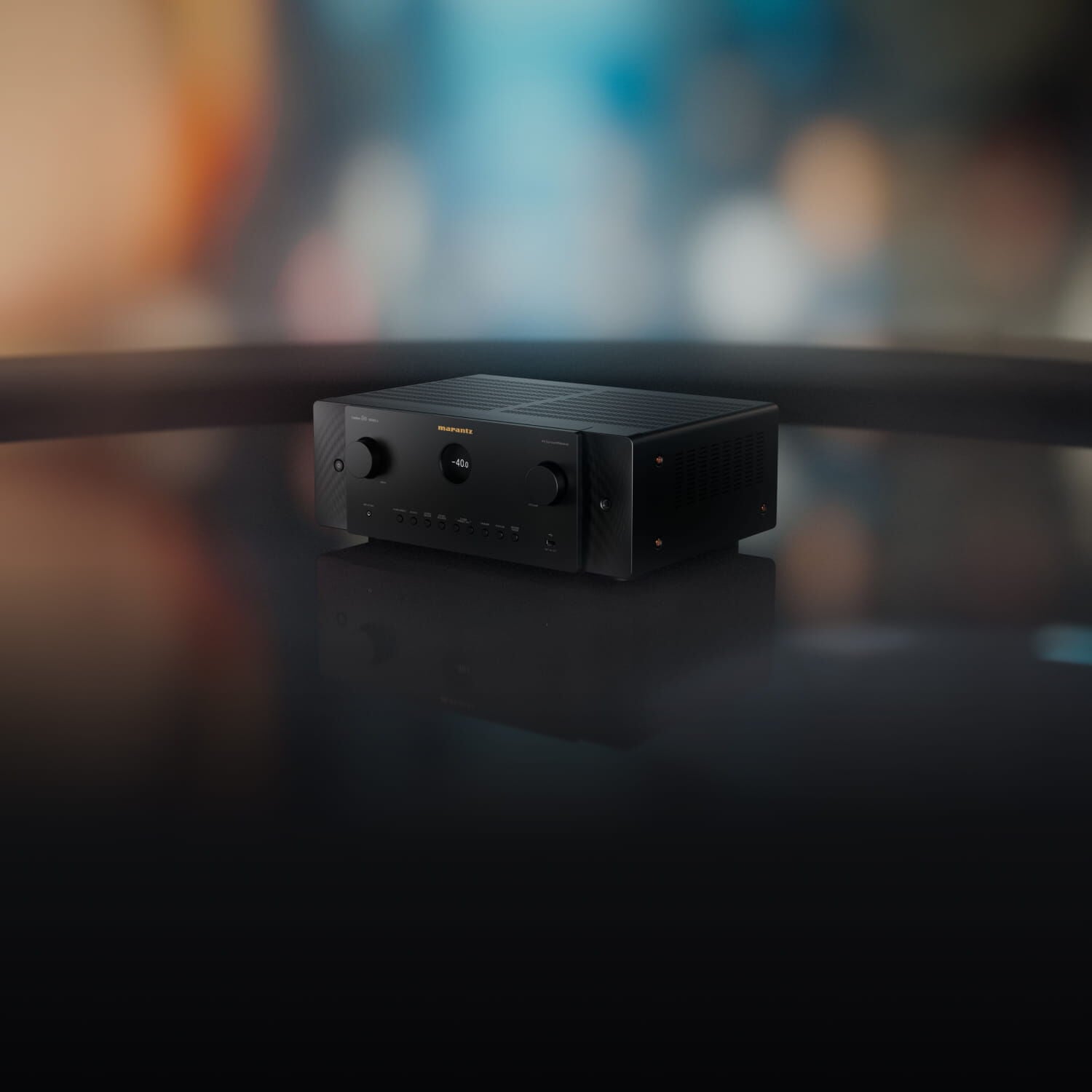 Marantz CINEMA 60 DAB SERIES 2 v černém provedení na lesklé desce, v pozadí rozostřená scéna s teplými a modrými světly