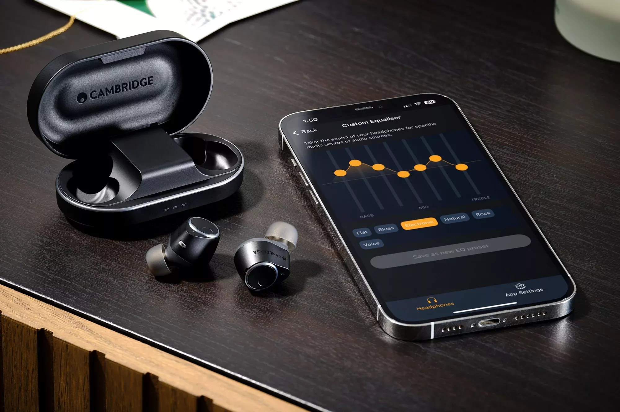 Sluchátka Cambridge Audio Melomania M100 vedle telefonu s aplikací Melomania Connect a sedmipásmovým ekvalizérem