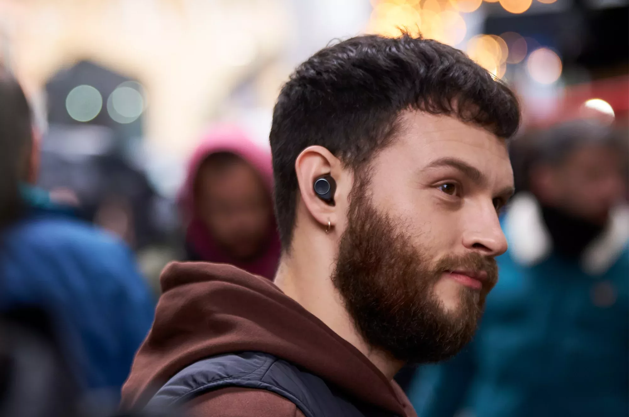 Muž nosí sluchátko Cambridge Audio Melomania M100 v rušné ulici plné lidí