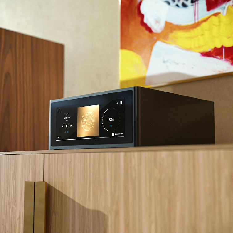 NAD M10 V3 na dřevěné polici v teplém světle, na displeji běží obal alba