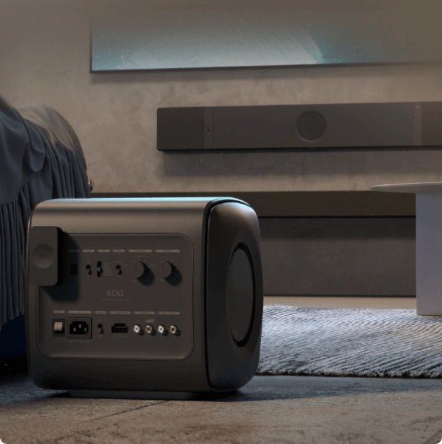 Černý subwoofer KEF na koberci v obývacím pokoji, na stěně za ním soundbar KEF XIO