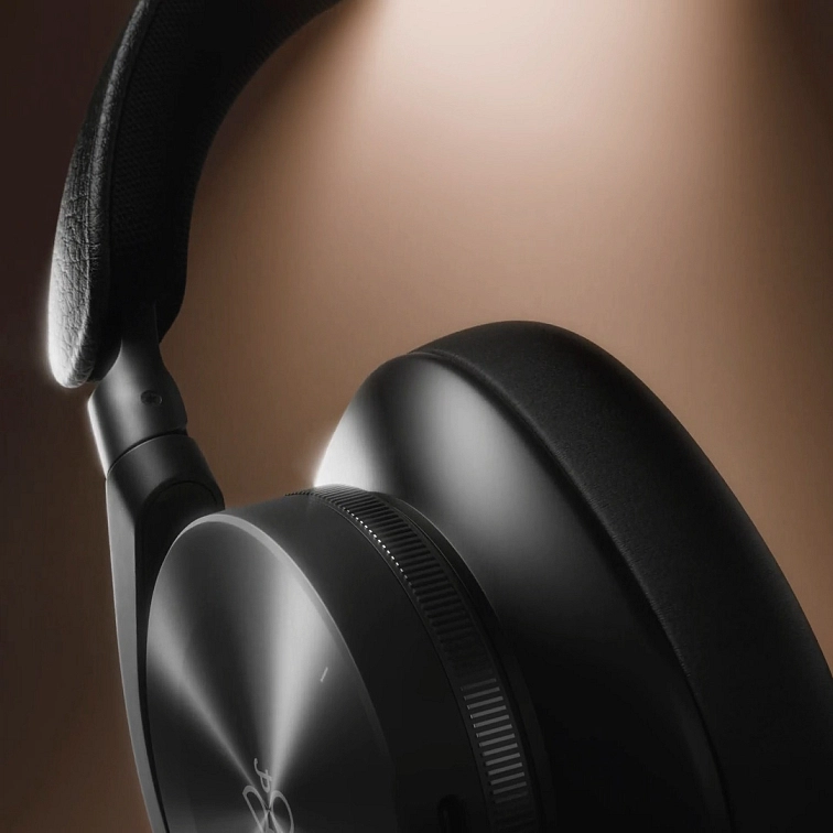 Detail černého náušníku Beoplay H95 s koženým páskem a hliníkovým ovládacím kolečkem