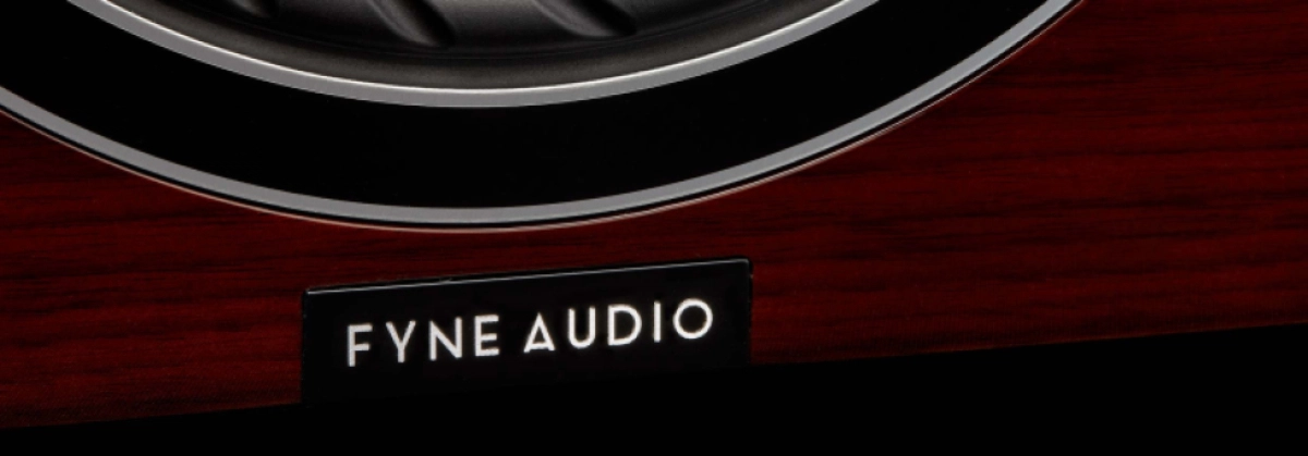 Detail loga FYNE AUDIO na lesklé mahagonové skříni středového reproduktoru F57SP-6 pod stříbrným lemem měniče