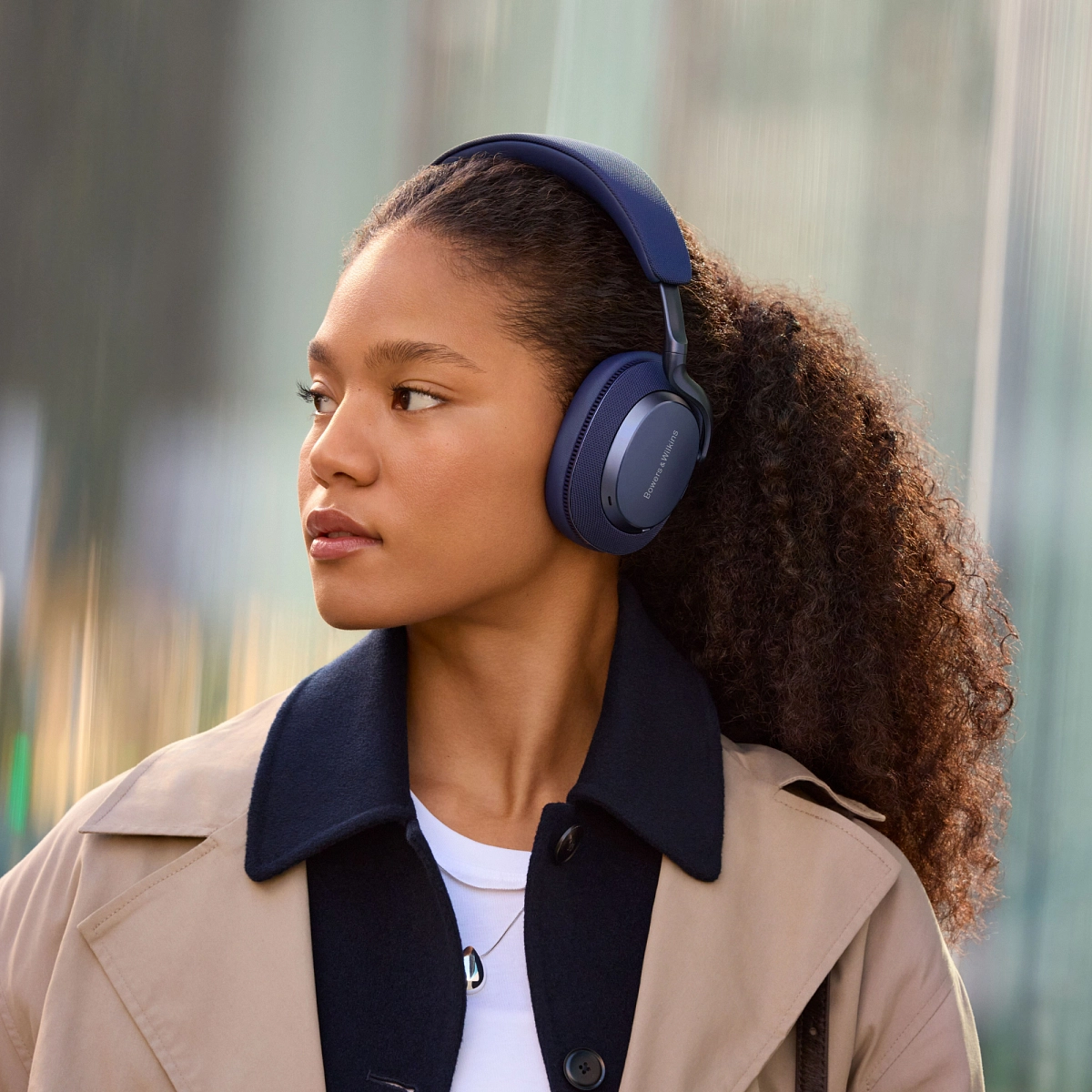 Žena v trenčkotu na ulici s náušními sluchátky Bowers & Wilkins Px7 S3 v provedení Indigo Blue