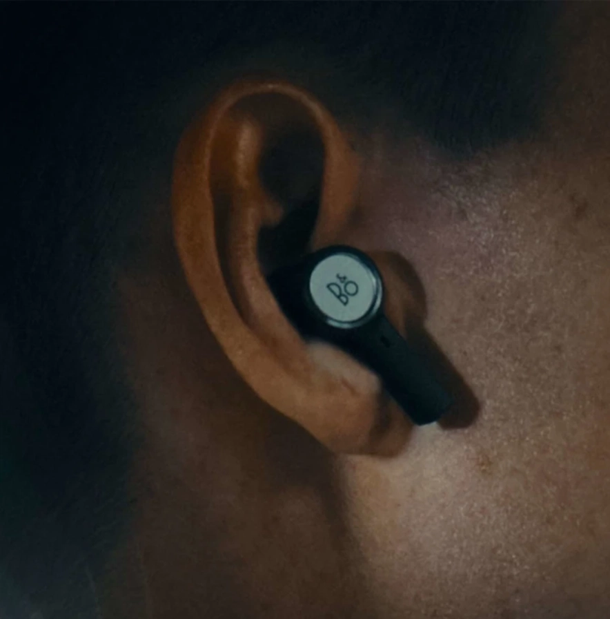 Detail ucha s nasazeným špuntem Beoplay Eleven a kruhovým logem Bang & Olufsen na dotykovém povrchu