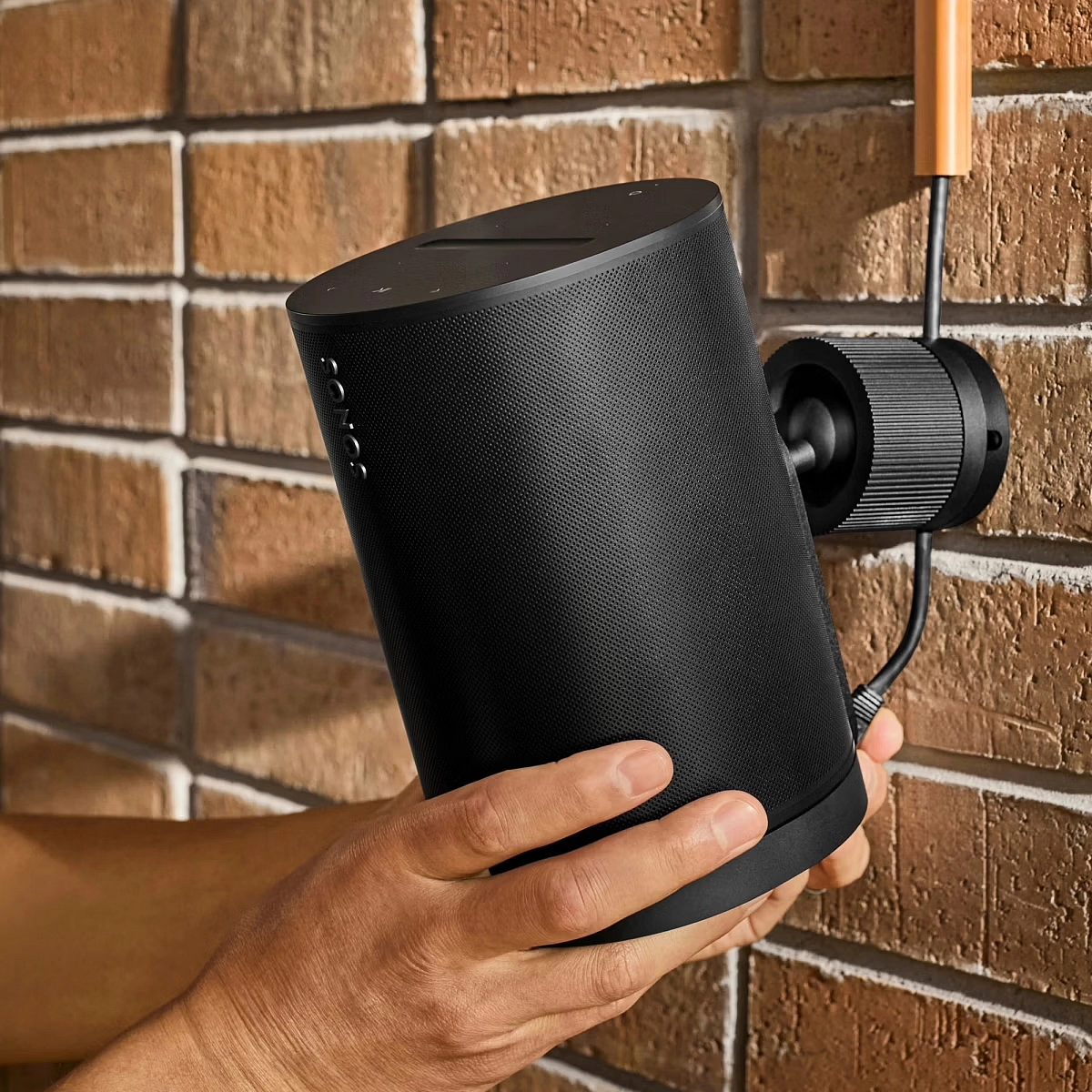 Černý reproduktor Sonos Era 100 Pro upevněný na cihlové zdi pomocí nástěnného držáku Surface Mount