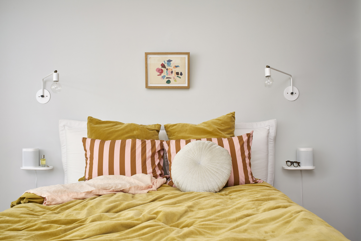 Dvě bílé Sonos Shelf Poličky po stranách postele v ložnici, na každé bílý reproduktor Sonos One