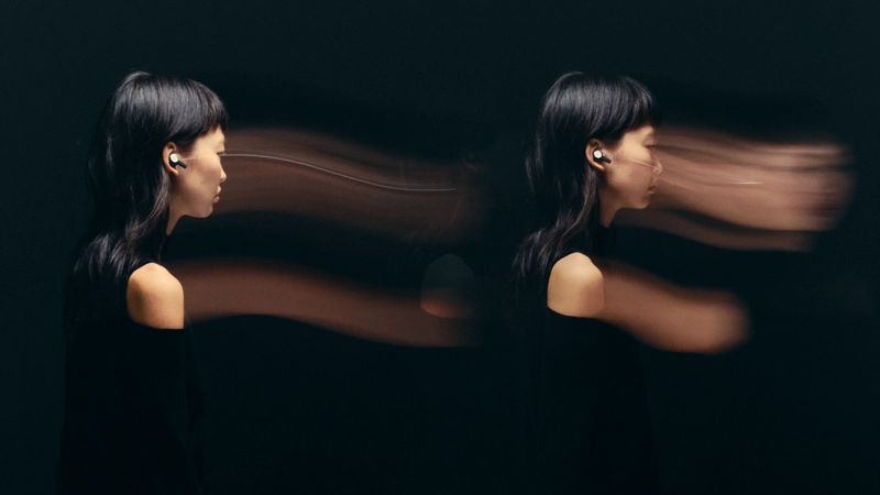 Žena z profilu s nasazenými špunty Beoplay Eleven na černém pozadí, motion blur kolem hlavy znázorňuje odpojení od okolí